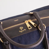 Close-up of the Weekend Bag's brown leather handles, gold-tone zippers and navy denim